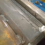 Flush ground FCAW weld on heavy structural steel component.